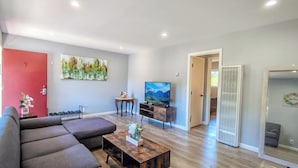 Uma sala de estar moderna com um sofá cinzento, uma mesa de centro de madeira, uma televisão de tela plana e um quadro na parede.