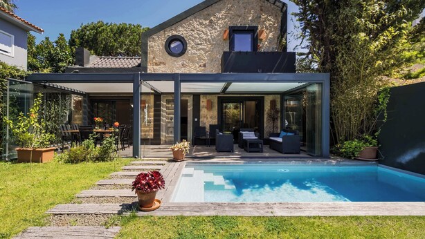 Ein modernes Haus mit Swimmingpool, Sitzgelegenheiten im Freien und einer Stein-Fassade.
