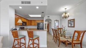 Una cocina moderna con armarios de madera, una isla central y un comedor con sillas de mimbre y una mesa de vidrio.