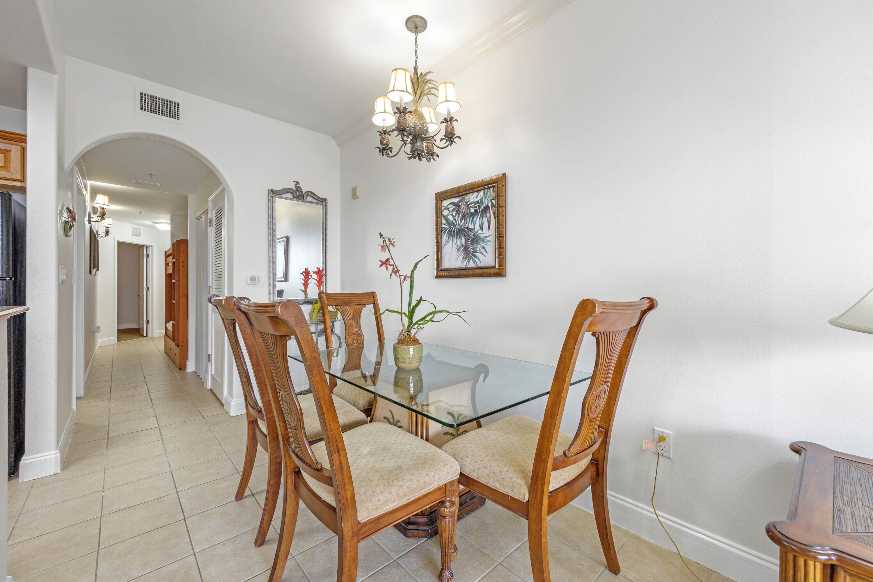 A dining area with a glass-top table, wooden chairs, a chandelier, and a framed picture on the wall.