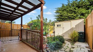 Un patio cubierto con un cerramiento de madera, un sendero de piedra y un cobertizo al fondo.