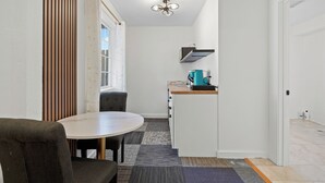 Cocina compacta con cafetera, comedor con mesa y sillas, y ventilador de techo.