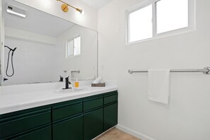 Ein modernes Badezimmer mit einem weißen Waschbecken, grünen Schränken, einem großen Spiegel und einem Handtuchhalter.