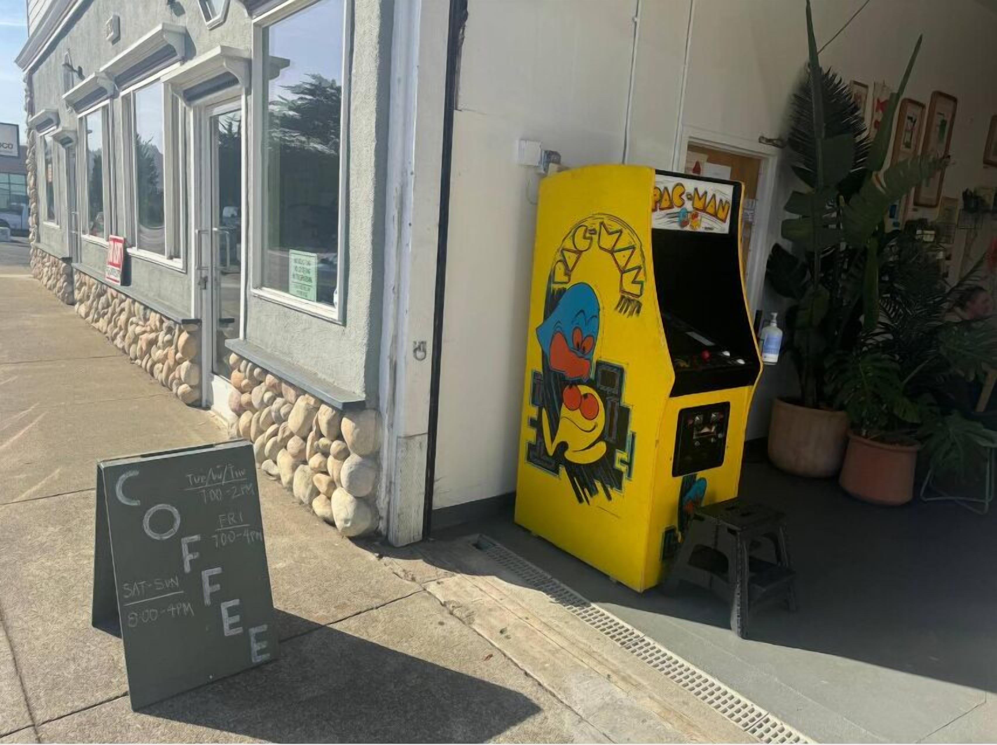 Uma cafeteria com uma máquina de arcade amarela do Pac-Man na frente.