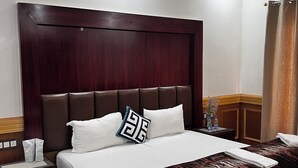 A hotel room with a large bed, wooden headboard, white bedding, and a patterned throw blanket. - LADAKH COUNTRY INN (Leh)