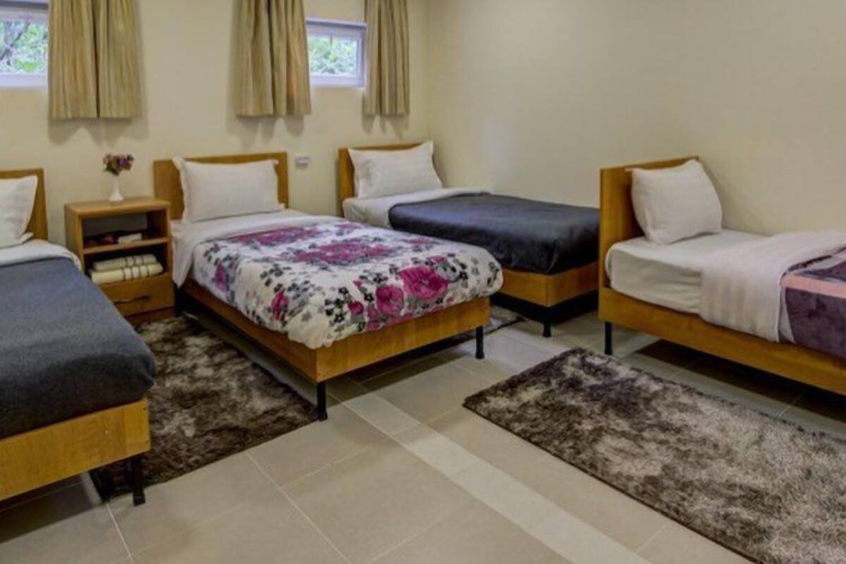 Une chambre avec trois lits, une petite table de chevet ornée d’un vase et une fenêtre avec des rideaux.
