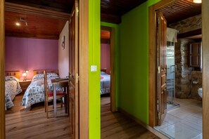 Una habitación con piso de madera, una cama con ropa de cama estampada, un escritorio con silla y un baño con pared de piedra.