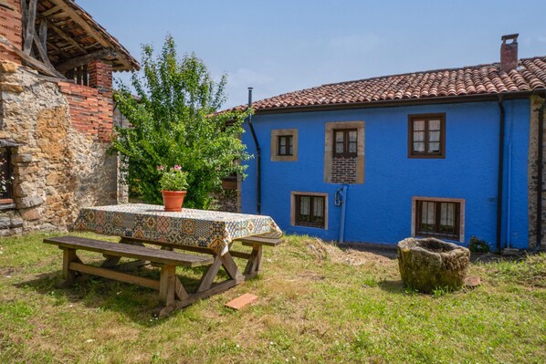 Un entorno rústico al aire libre con una mesa de picnic de madera, una planta en maceta y un muro de piedra.