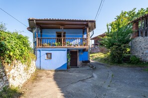 Un edificio de dos pisos con un balcón, una pared de piedra en un lado y una entrada pavimentada.