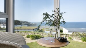 Un balcon avec vue sur la mer, une table en bois avec deux verres et une plante, et une paire de jumelles.