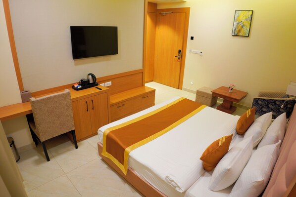 A hotel room with a bed, a desk, a chair, a television, and a door.