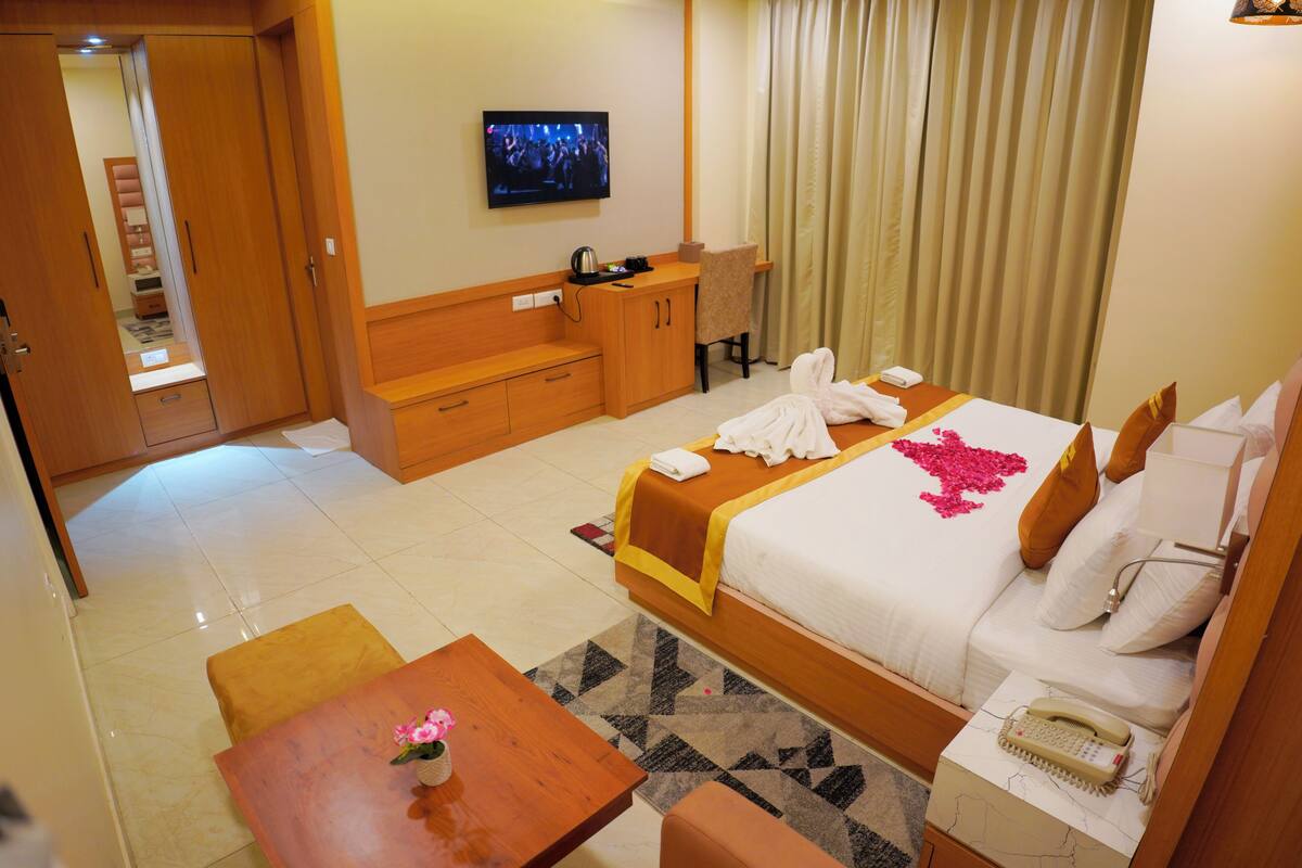 Quarto de hotel com cama, escrivaninha, televisão, banheiro e chuveiro.