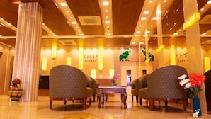 A lobby with a reception desk, two armchairs, a vase with flowers, and a decorative pillar. - Hotel Cheer Royale (Bareilly)