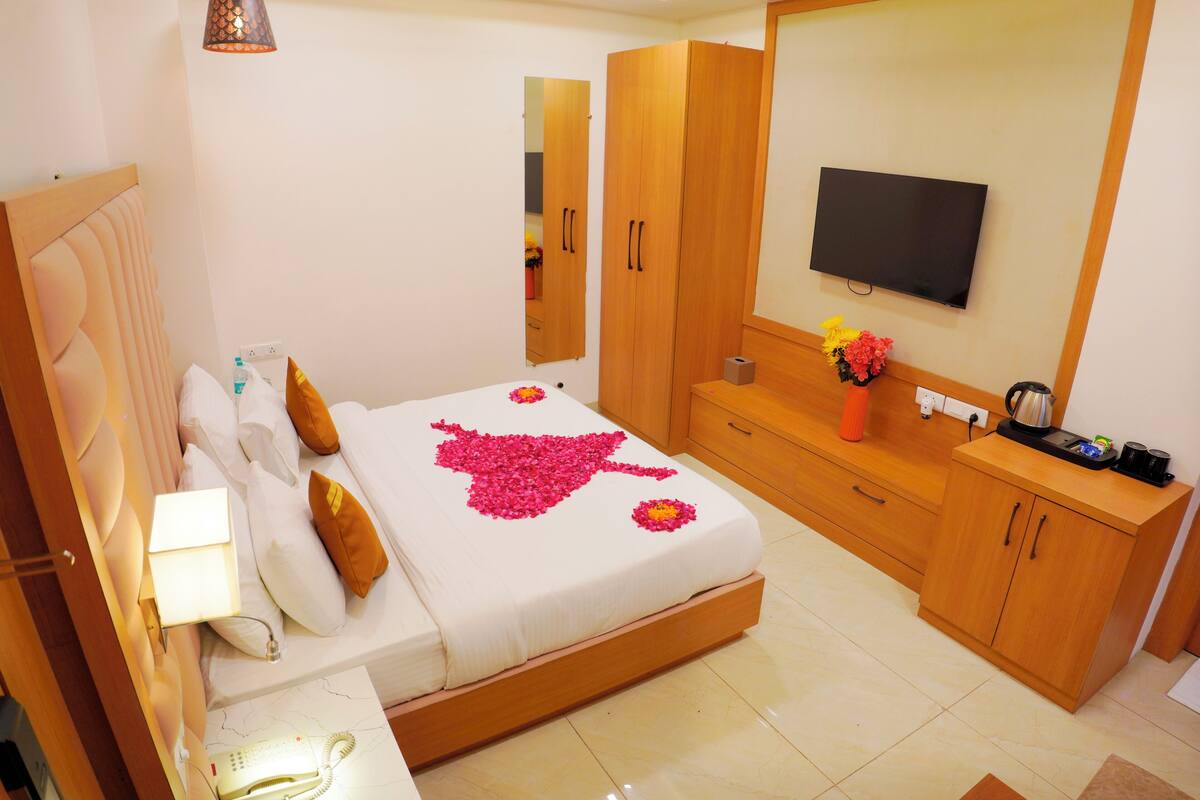 Quarto de hotel com cama, guarda-roupa de madeira, televisão e mesa de cabeceira com abajur.