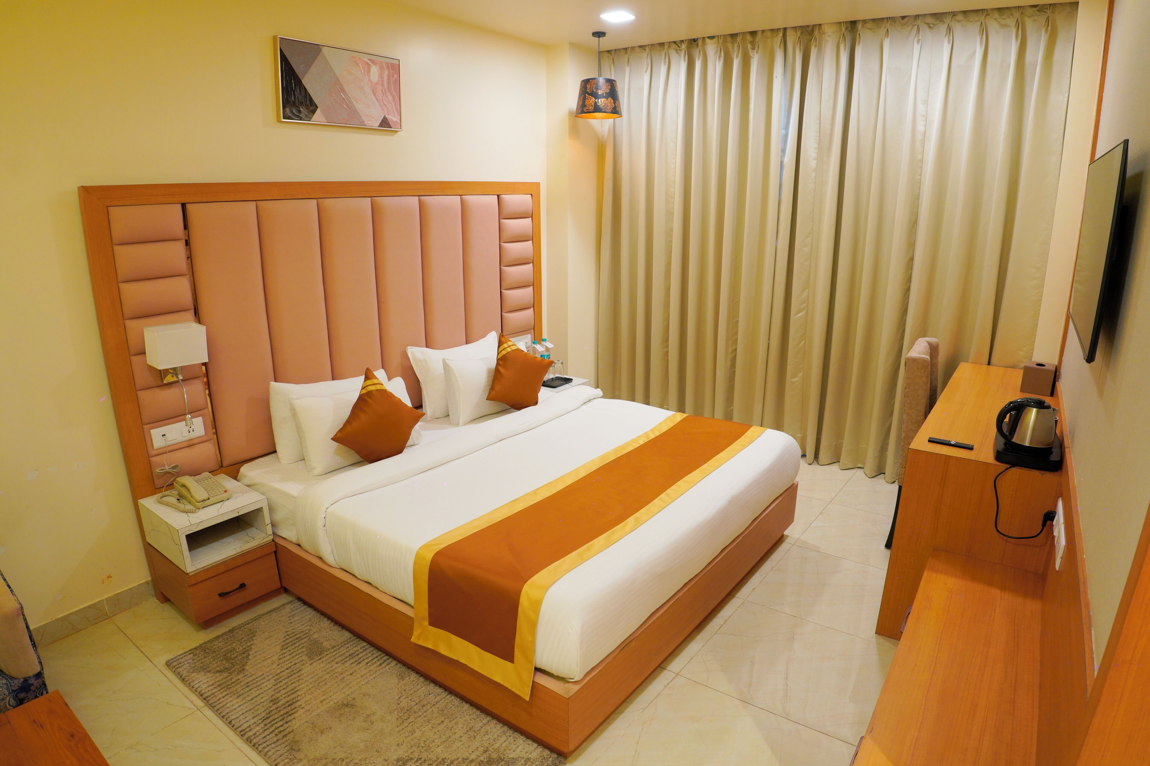 A hotel room with a large bed, a bedside table with a lamp, a desk with a chair, and a television on the wall.