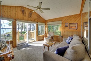 Ein gemütliches Blockhaus-Interieur mit Holzvertäfelung, einem Deckenventilator, einem großen Fenster und Blick ins Freie.