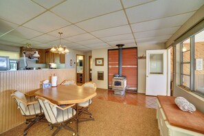 A kitchen with a dining table and chairs, a stove, and a window with blinds. - Dock & Fire Pit: Lakefront Cottage in Gould City! (Gould City)