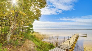 A wooden dock extending into calm water, surrounded by trees and vegetation. - Dock & Fire Pit: Lakefront Cottage in Gould City! (Gould City)