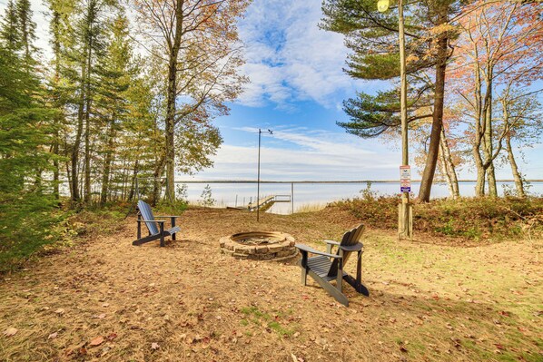 A lakeside park with Adirondack chairs, a fire pit, and a warning sign about shallow water. - Dock & Fire Pit: Lakefront Cottage in Gould City! (Gould City)