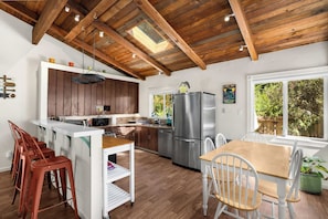 A kitchen with wooden beams, a stainless steel refrigerator, and a dining area with a table and chairs. - Hot Tub Retreat Near Russian River • BBQ • Family Friendly (Guerneville)