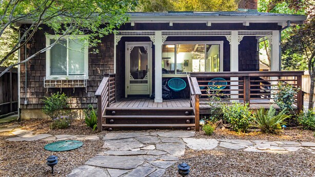 Een houten huis met veranda, een pad van stenen en een kleine tuin.
