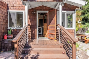A wooden house with a porch, a staircase, and a door leading to an interior space. - Hot Tub Retreat Near Russian River • BBQ • Family Friendly (Guerneville)