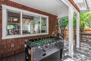 A wooden deck with a foosball table and a window overlooking a backyard. - Hot Tub Retreat Near Russian River • BBQ • Family Friendly (Guerneville)