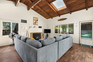 A modern living room with a large sectional sofa, a fireplace, a flat-screen TV, and a ceiling fan. - Hot Tub Retreat Near Russian River • BBQ • Family Friendly (Guerneville)