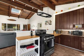 A modern kitchen with a central island, wooden cabinets, and a hanging light fixture. - Hot Tub Retreat Near Russian River • BBQ • Family Friendly (Guerneville)