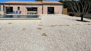 A building with a swimming pool, lounge chairs, and a gravel-covered area.