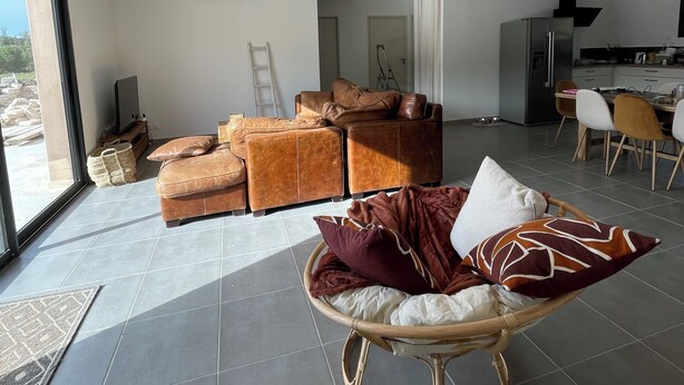 A spacious living area with a sofa set, a wicker chair, and a dining area with chairs and a table.