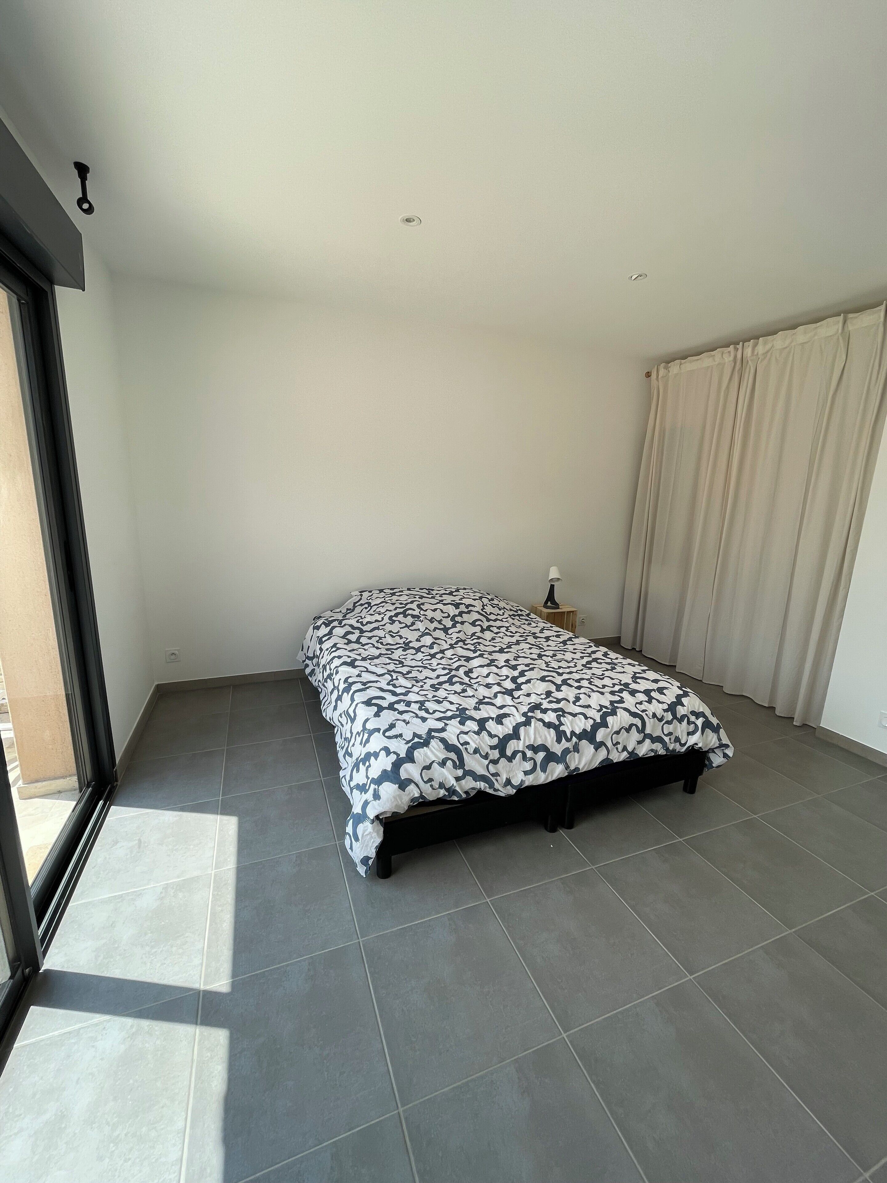 Une chambre à coucher avec un lit, une table de chevet, une lampe et une fenêtre avec des rideaux.