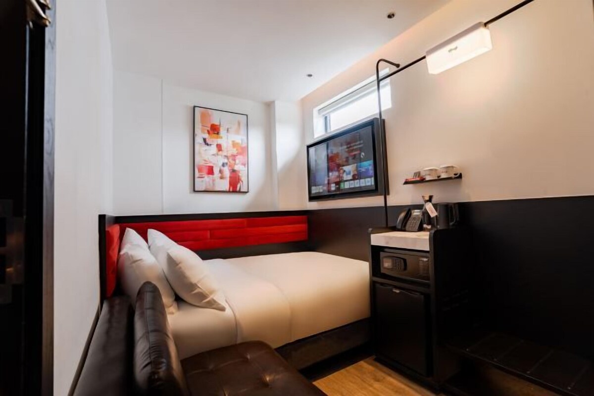 A modern bedroom with a bed, a desk, a television, and a window.