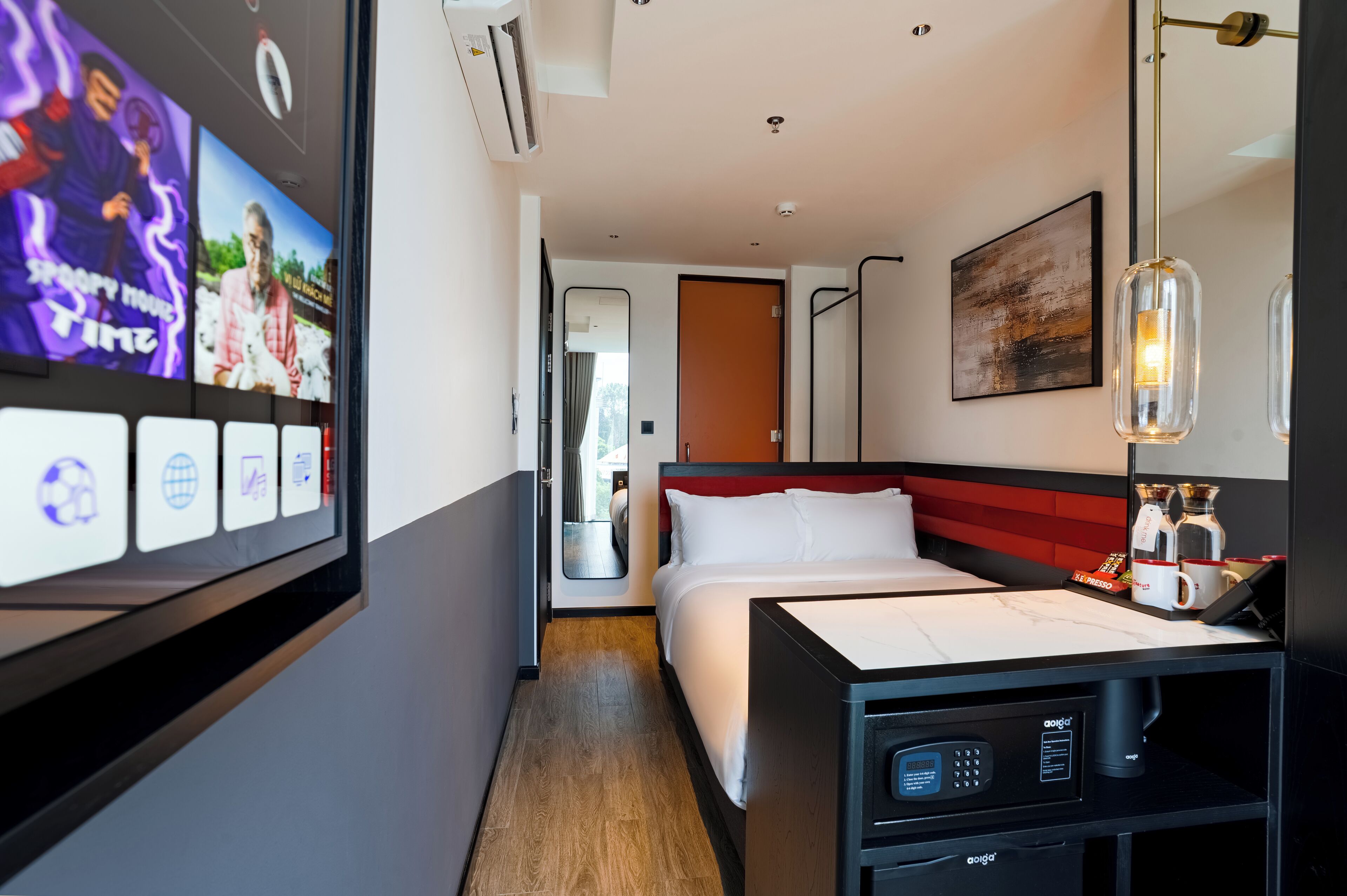 Quarto de hotel com cama, televisão na parede, máquina de café e mesa de cabeceira.