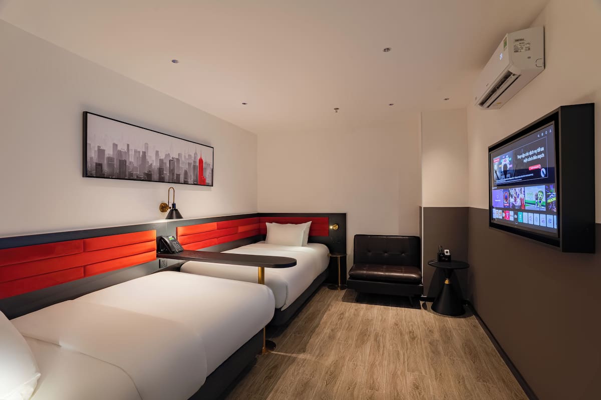 Ein Hotelzimmer mit zwei Betten, einer roten Akzentwand, einem wandmontierten Fernseher und einem Stadtbild.