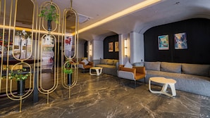 A modern lobby with a sofa, chairs, a coffee table, and decorative mirrors. - The Signature Hotel Saigon (Ho Chi Minh City)