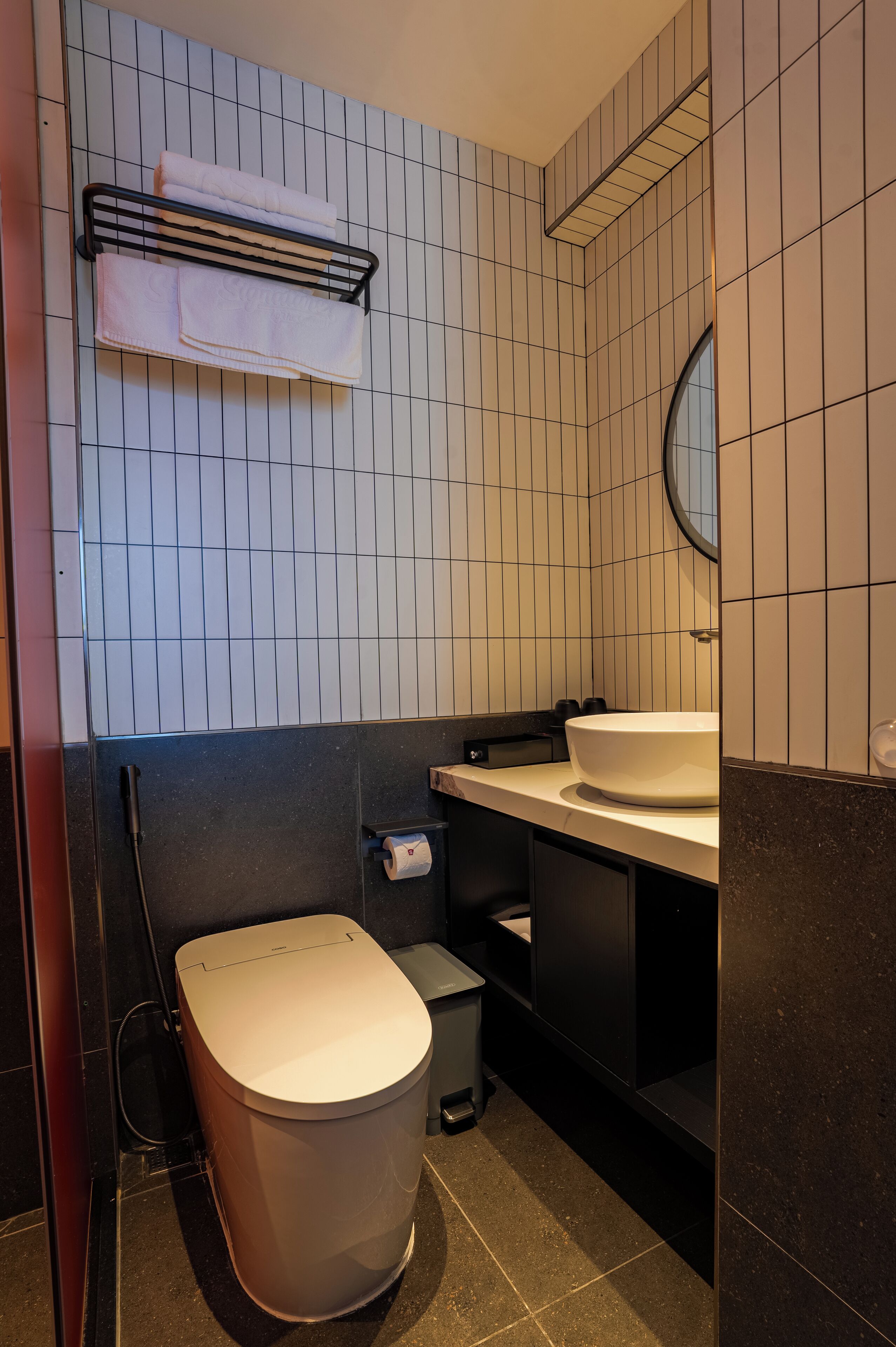 Ein modernes Badezimmer mit einem weißen Waschbecken, einer schwarzen Toilette und einem Handtuchhalter mit zwei Handtüchern.