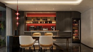 A modern kitchen with a bar area, featuring a marble countertop, two bar stools, and a red pendant light. - The Signature Hotel Saigon (Ho Chi Minh City)