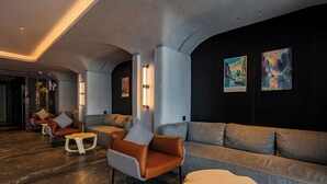 A modern lobby with a dark wall, a grey sofa, leather armchairs, and a marble floor. - The Signature Hotel Saigon (Ho Chi Minh City)