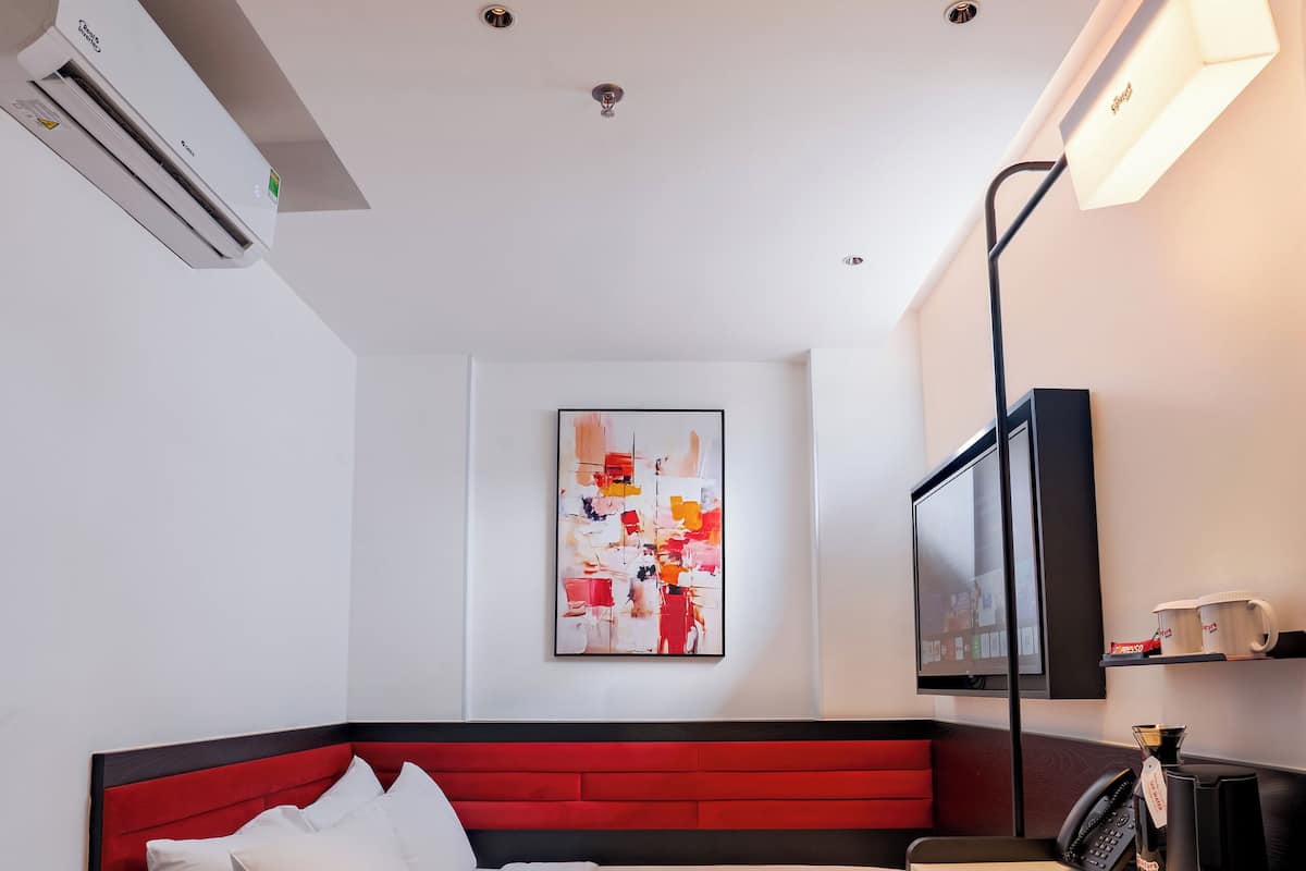 Ein modernes Hotelzimmer mit einem Bett mit rotem Kopfteil, einer schwarzen Ledersofa, einem Flachbildfernseher, einer Kaffeemaschine und einem Wandbild.
