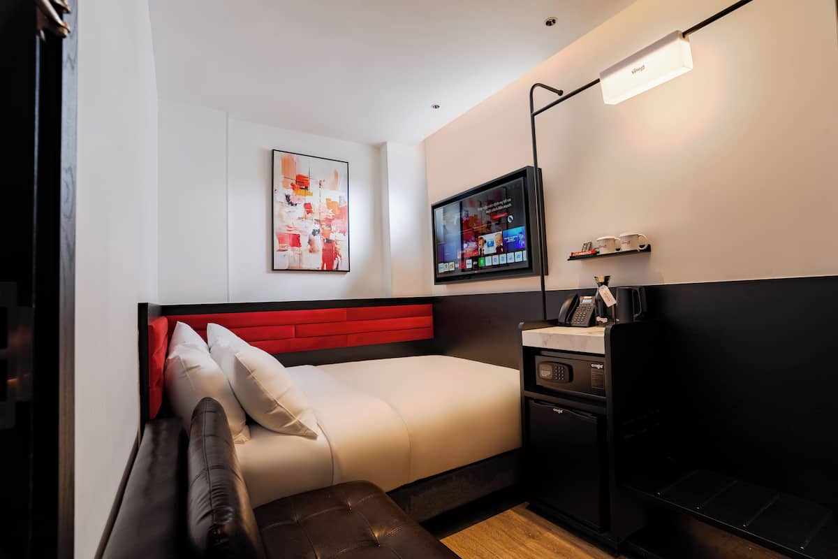 Ein modernes Hotelzimmer mit einem Bett, einem Fernseher, einer Kaffeemaschine und einem kleinen Regal mit Tassen.