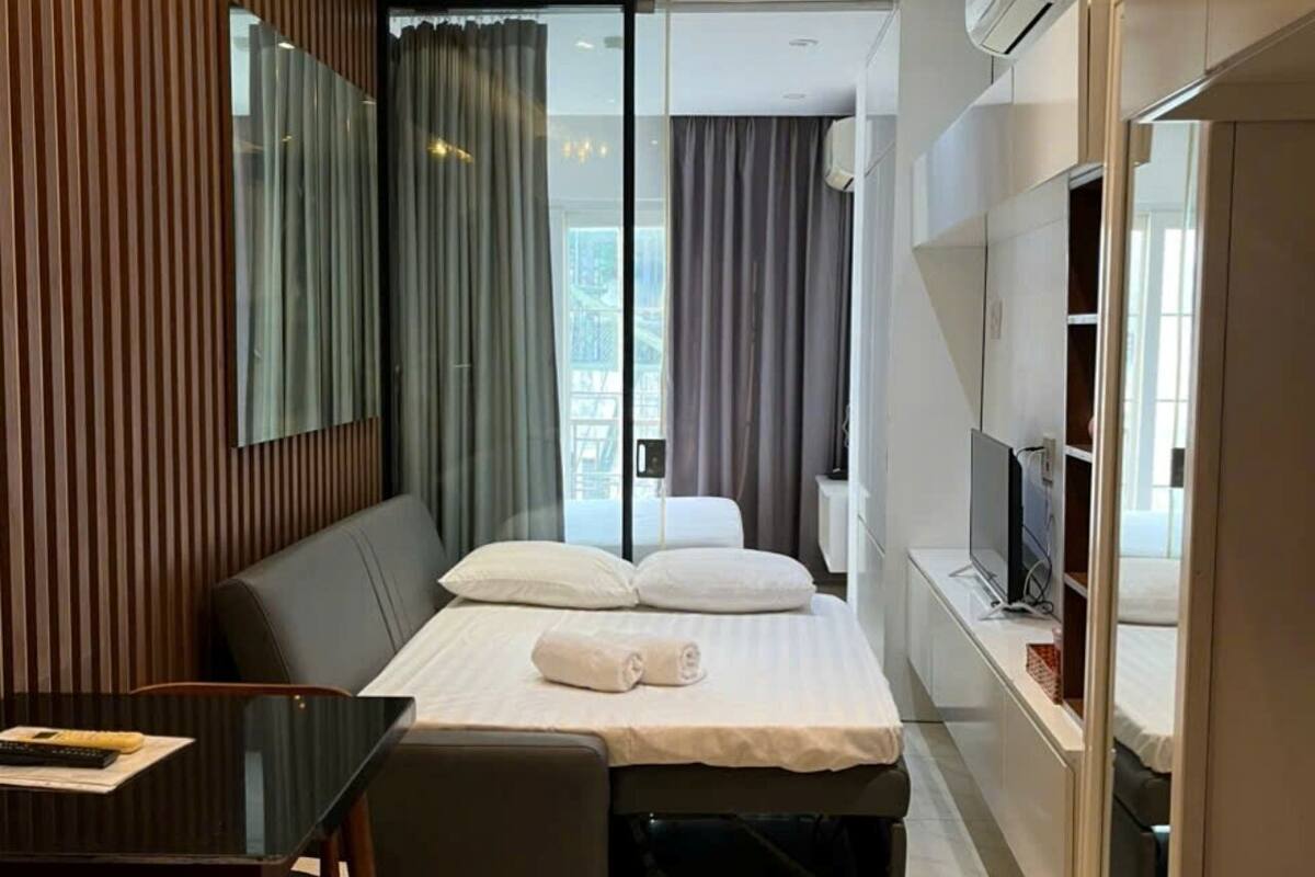 Una habitación de hotel moderna con una cama, una mesita, un banco, un televisor y un equipo de aire acondicionado.