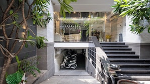 A modern indoor staircase leading to a glass door entrance, surrounded by potted plants and a scooter.
