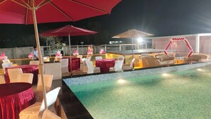A poolside area with tables and chairs, a pool, and umbrellas. - Shubh Shaleen Springs by Nexottel (Bhopal)