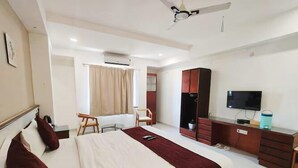 A hotel room with a bed, a desk, a chair, a TV, and an air conditioning unit. - Shubh Shaleen Springs by Nexottel (Bhopal)