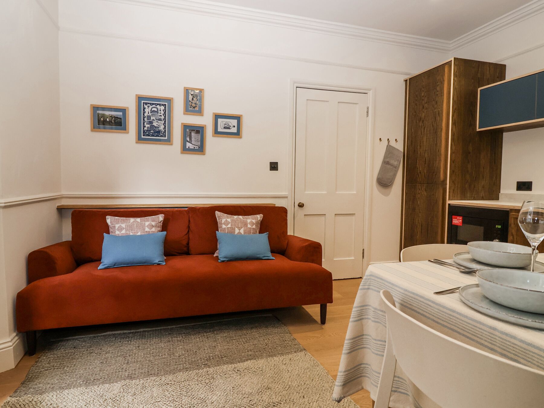 Ein Wohnzimmer mit einem roten Sofa, einem Esstisch mit weißem Tischlauf und gerahmten Bildern an der Wand.