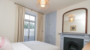 Un dormitorio con cama, chimenea, ventana con cortinas y espejo en la pared.