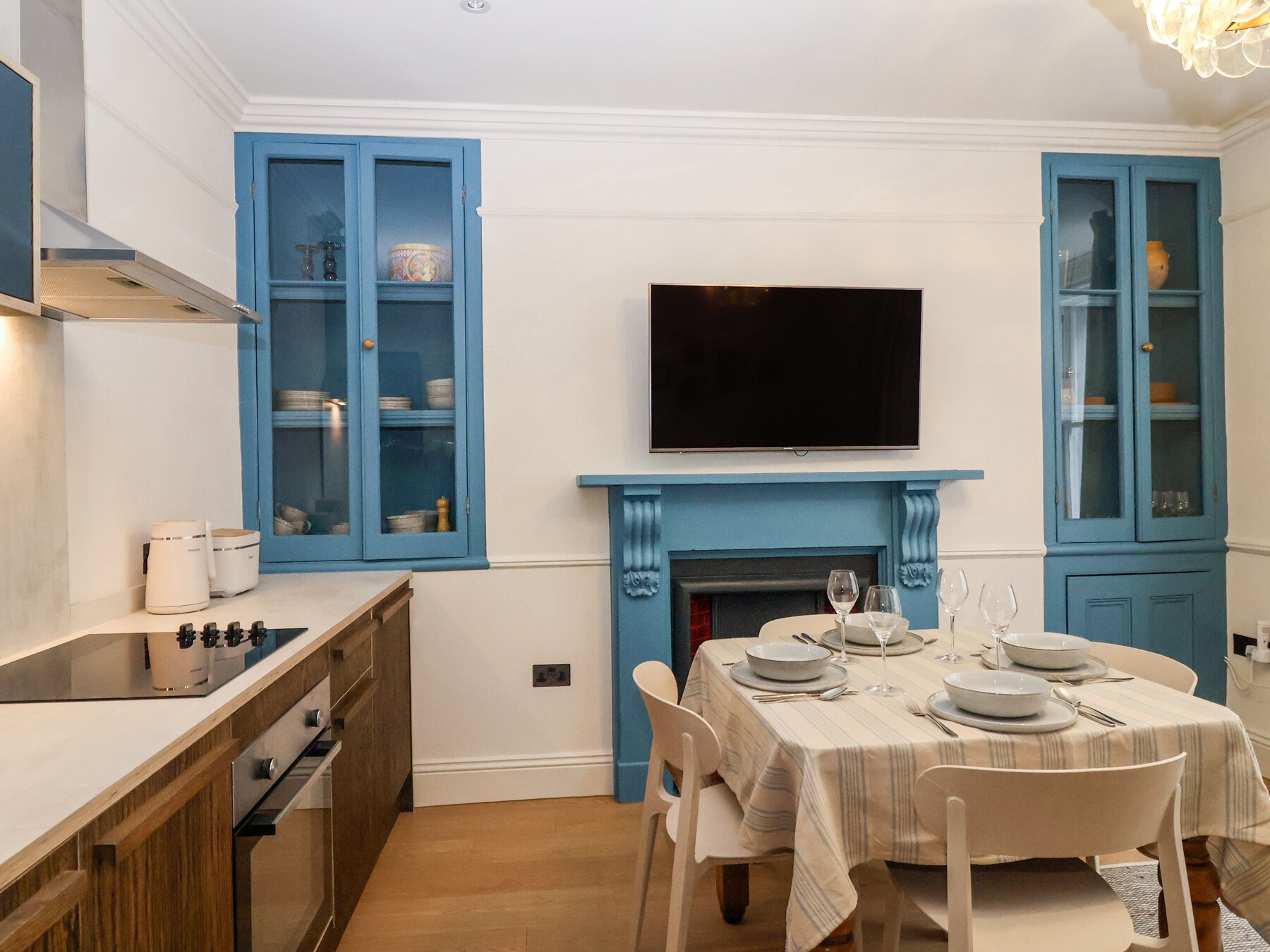 A dining area with a table set for four, a television above a fireplace, and blue cabinets with glass doors.