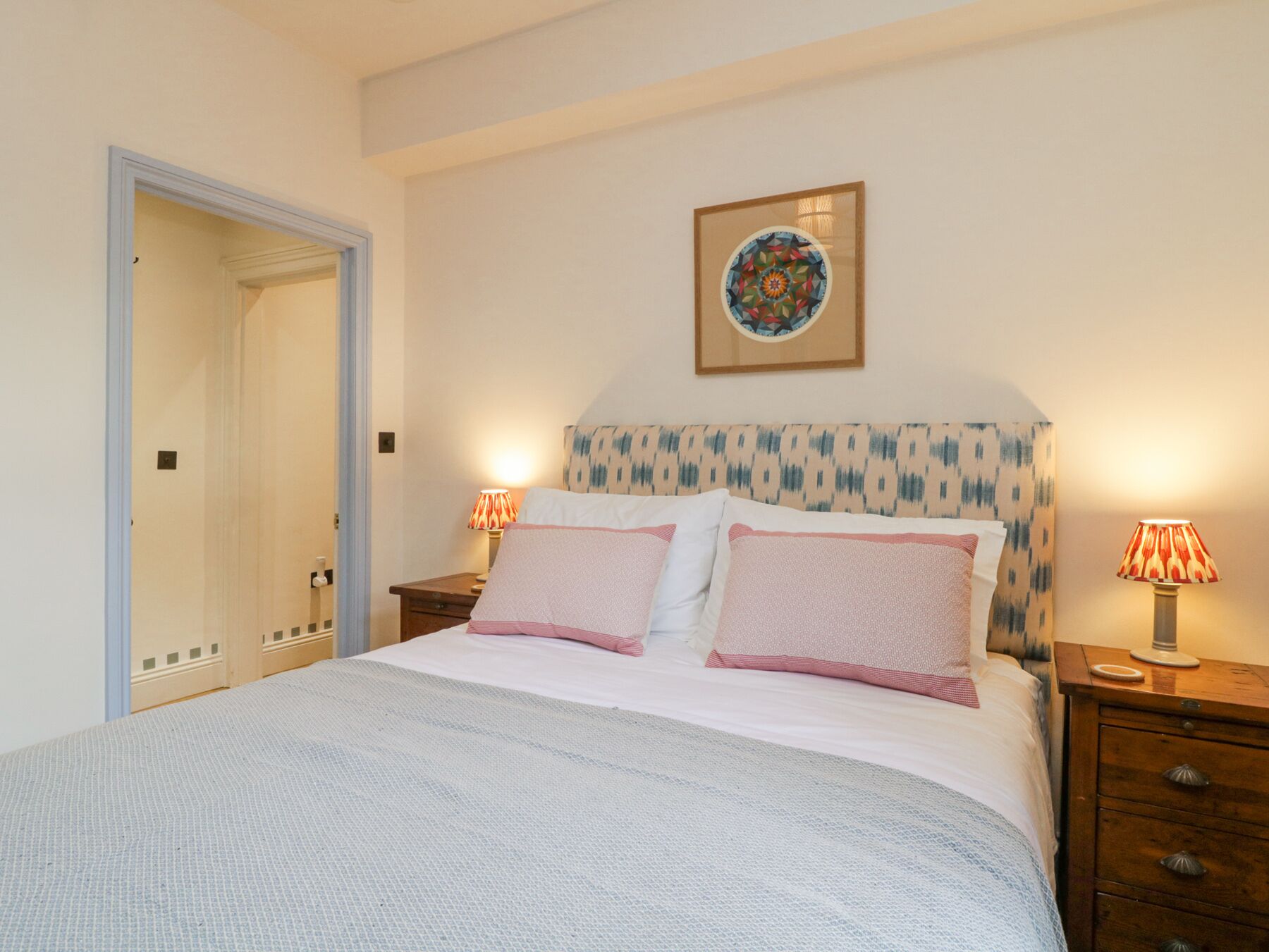 Une chambre à coucher comprenant un lit, deux tables de chevet, une porte et une œuvre d’art accrochée au mur.