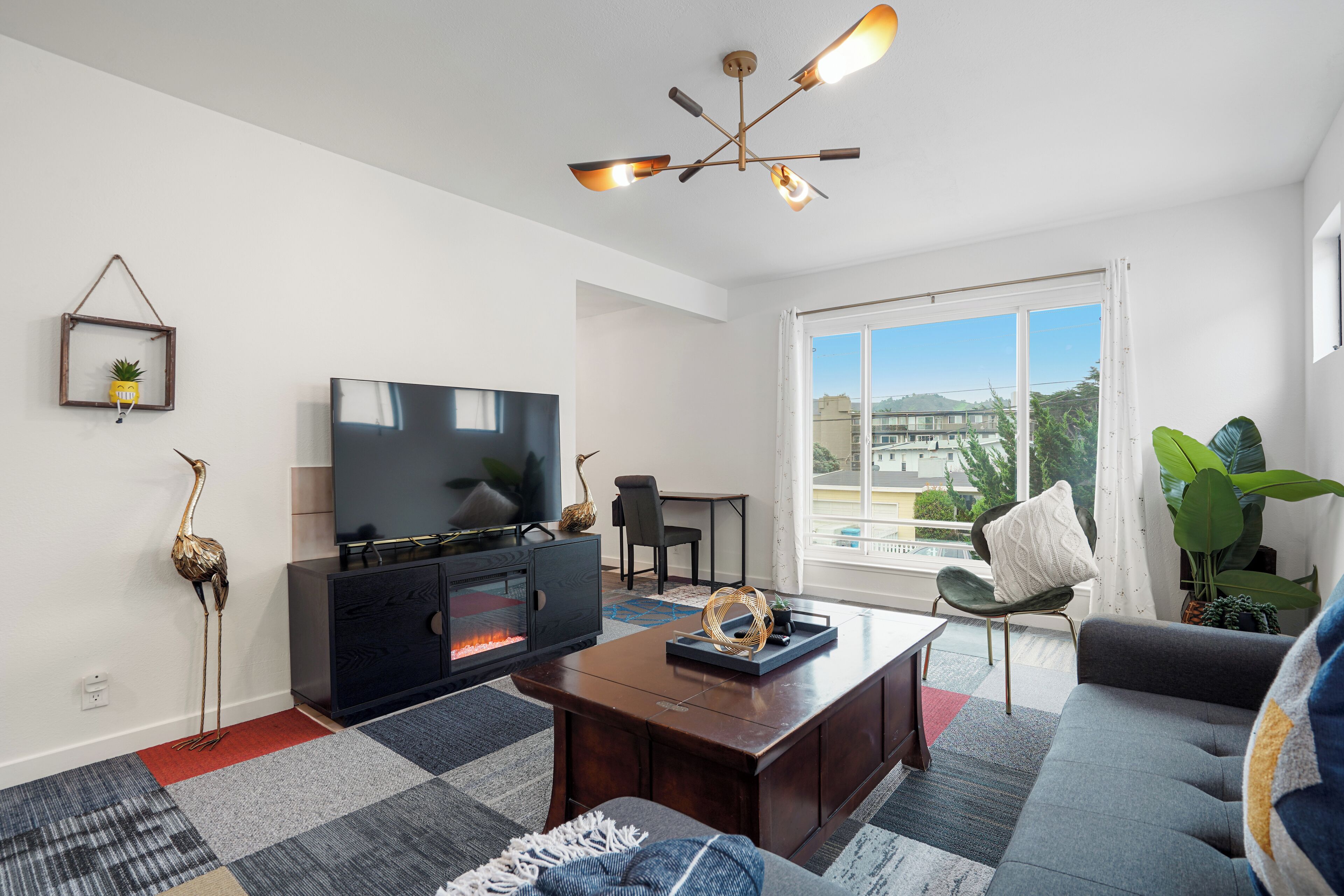 Una sala de estar moderna con televisor de pantalla plana, chimenea, mesa de centro, sofá y un amplio ventanal con vistas a la ciudad.